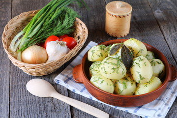 Boiled potatoes in a clay bowl on the wooden table with vegetables.