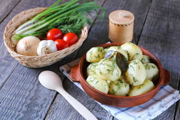 Boiled potatoes in a clay bowl on the wooden table with vegetables.