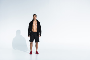 sportive mixed race man in black sports jacket, shorts and red sneakers on white background