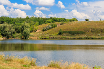 Summer landscape with beautiful lake, green meadows, hills, trees and blue sky