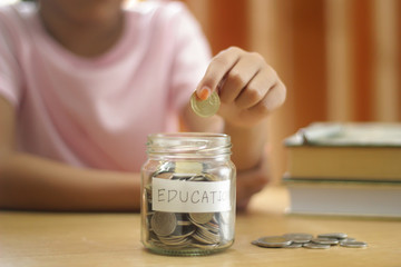 Hand's girl holding coins putting in glass with books on the table.saving for education concept.