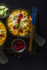 laks with pumpkin and coconut milk, rice noodles, broccoli and pomegranate seeds in portioned black plates onlaksa with pumpkin and coconut milk, rice noodles, broccoli and pomegranate seeds 