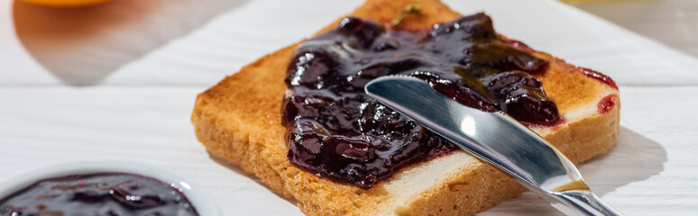 panoramic shot of toast with jam near knife on white