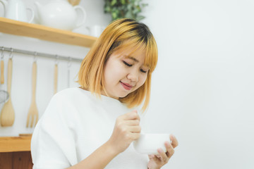 Attractive beautiful asian woman enjoying warm coffee in the kitchen at her home. Asian female wearing comfortable sweater holding a cup of coffee. lifestyle asia woman at home concept.