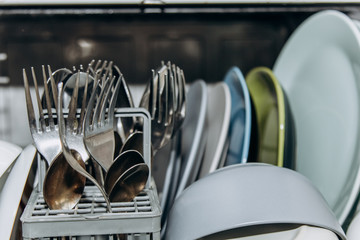 open dishwasher close up clogged with clean washed dishes. dry cutlery closeup. spoons forks. mugs,...