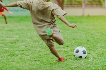 Obraz premium Asian boys practice kicking the ball to score goals in the public football field.
