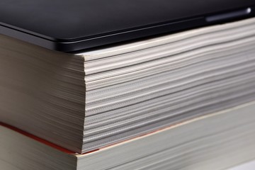 Laptop computer stacked upon thick soft cover book