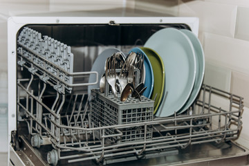 open dishwasher close up clogged with clean washed dishes. dry cutlery closeup. spoons forks. mugs, plates. household appliances in the kitchen
