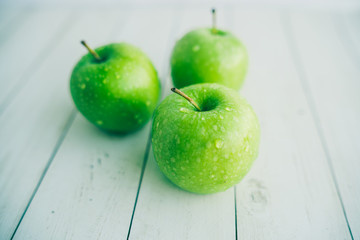 Juicy green apples on white background. Three apples with water drops on white wooden background