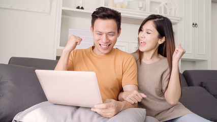 Asian couple using laptop for search web in living room at home, sweet couple enjoy love moment while lying on the sofa when relax at home. Lifestyle couple relax at home concept.