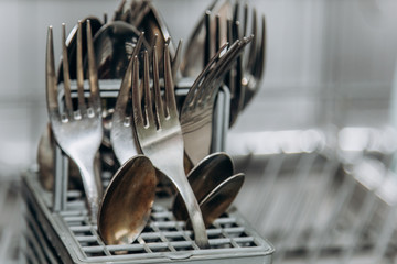clean dry forks and spoons in an open dishwasher closeup. cutlery compartment close-up. household appliances in the kitchen