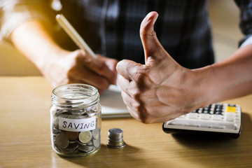 A businessman show thumb and holding coins putting into the glass. concept saving money and finance accounting.