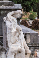 The statue of man and Grim Reaper on the background of grave on the Montjuic Cemetery closeup, Barcelona, Catalonia, Spain
