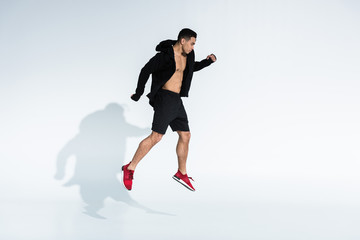 Fototapeta na wymiar handsome mixed race man in black sports jacket, shorts and red sneakers jumping on white