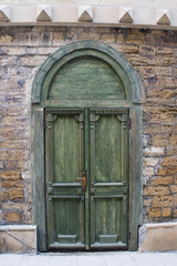 Fototapeta na wymiar Old beautiful green wooden door in a stone wall in the form of an arch.