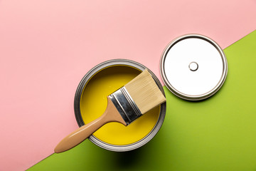 top view of tin with yellow paint and brush on pink and green surface