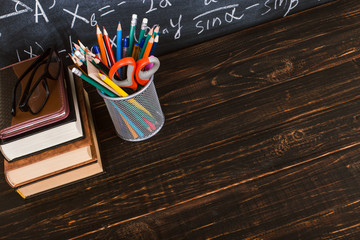 Books and stand for pens on a wooden table, against the background of a chalk board with formulas. Teacher's day concept and back to school.