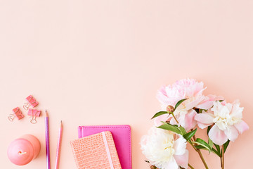 Blogger or freelancer workspace with notebook and light pink peonies on a pink background