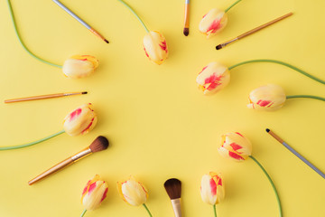 Flat lay composition with cosmetic products for makeup and yellow tulips on a yellow background