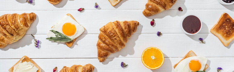 panoramic shot of sweet croissants and tasty toasts near dried flowers on white