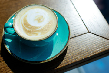Cappuccino with frothy foam. Coffee in blue cup on wooden table. Top view with copyspace for your text. 