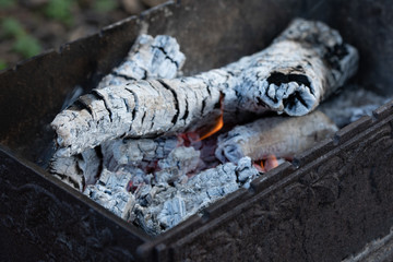 Burning embers in cast iron grill. Preparation of coal for barbecue. Firewood in ash, closeup
