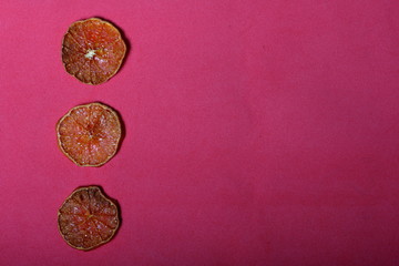 Tangerines are cut into slices and dried to decorate desserts. On a pink background.