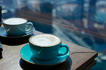 Cappuccino with frothy foam. Coffee in blue cup on wooden table near the window.