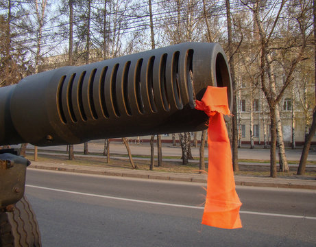 The barrel of a gun with a tied red ribbon on the muzzle brake. Road, urban environment. The concept of the holiday "Victory Day"