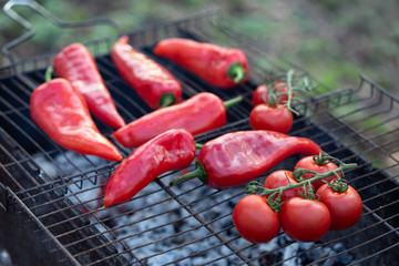 Red tomatoes on branches and red bell peppers on the grill. Cooking process, close up