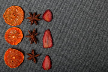 Tangerines are cut into slices and dried to decorate desserts. Nearby are stars of anise and strawberry slices. On a gray background.