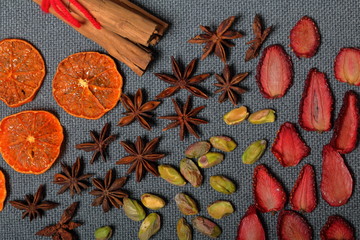 Dried tangerines and strawberries, cut into pieces to decorate the dessert. Nearby are pistachios, anise and cinnamon sticks tied with red thread. On a gray background.