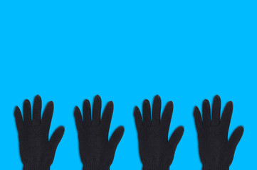 Fototapeta premium Horizontal row of four black warm woolen gloves on blue background with copy space for your text. Top view