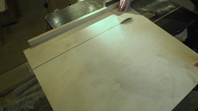 Medium shot side view of mature furniture maker using circular saw to make cuts in wooden plank in workshop light with sunlight