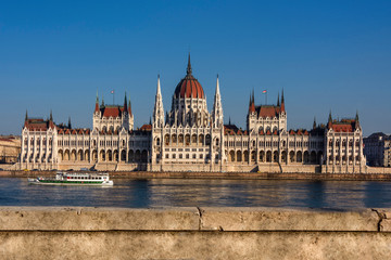 Fototapeta premium Węgry, Budapeszt: słynny budynek parlamentu Węgier w słoneczne popołudnie w centrum stolicy Węgier z wodą Dunaju, statkiem wycieczkowym i błękitnym niebem - polityka architektoniczna
