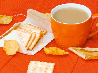 Cup of coffee, dry cracker cookies and dry leaves on an orange background. Autumn background, flat lay. Autumn composition. Autumn mood, top view. Cup of autumn coffee and yellow dry leaves.