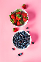 Strawberries and blueberries in bowls on pink background.