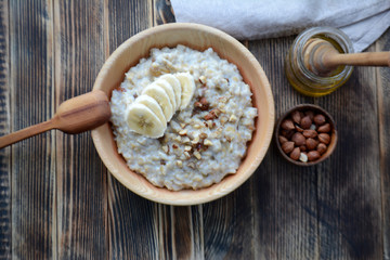 Oatmeal porridge with bananas, nuts and honey in a wooden bowl Top view 