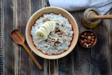 Oatmeal porridge with bananas, nuts and honey in a wooden bowl Top view 