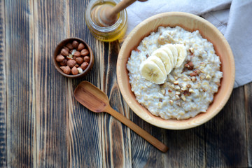 Oatmeal porridge with bananas, nuts and honey in a wooden bowl Top view Copy space