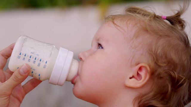 Cute girl drinking milk from a bottle in the garden