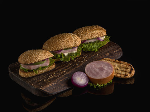  Sandwiches with ham, avocado, cheese and greens on a dark background