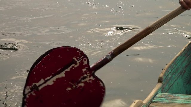 Close up of a red, heart-shaped paddle propelling a wooden boat with faded green paint