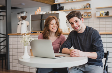 Two young people working with a laptop in a cafe and drinking coffee