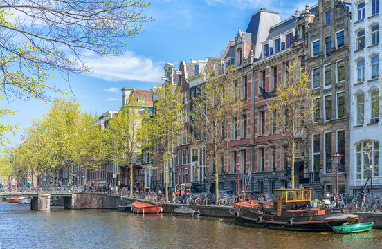 Amsterdam, Netherlands - April 09, 2019: Classic bicycles and historical houses in old Amsterdam. Typical street in Amsterdam with canal and colorful houses in the Dutch style on the Sunset.