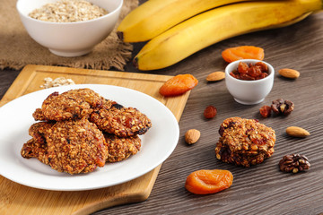 homemade  oat flakes cookies chips and ingredients banana walnuts almonds raisin dried apricots on wooden table close up