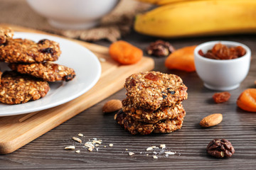 healthy oat flakes cookies  and ingredients banana walnuts almonds raisin dried apricots on wooden board   soft focus