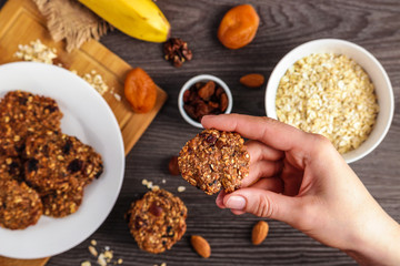 woman hand holding homemade vegetarian oat cookie chip top view .ingredients on wooden table soft focus