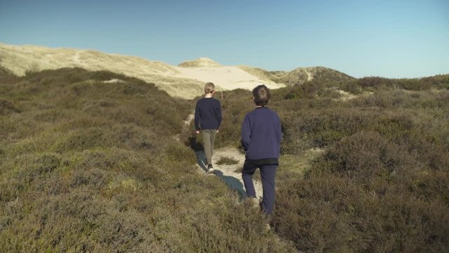 Two young boys walking through beach vegetation