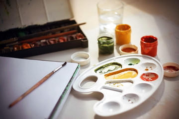 On the table there are watercolor paints in a vintage box, a large notebook for drawing on a...